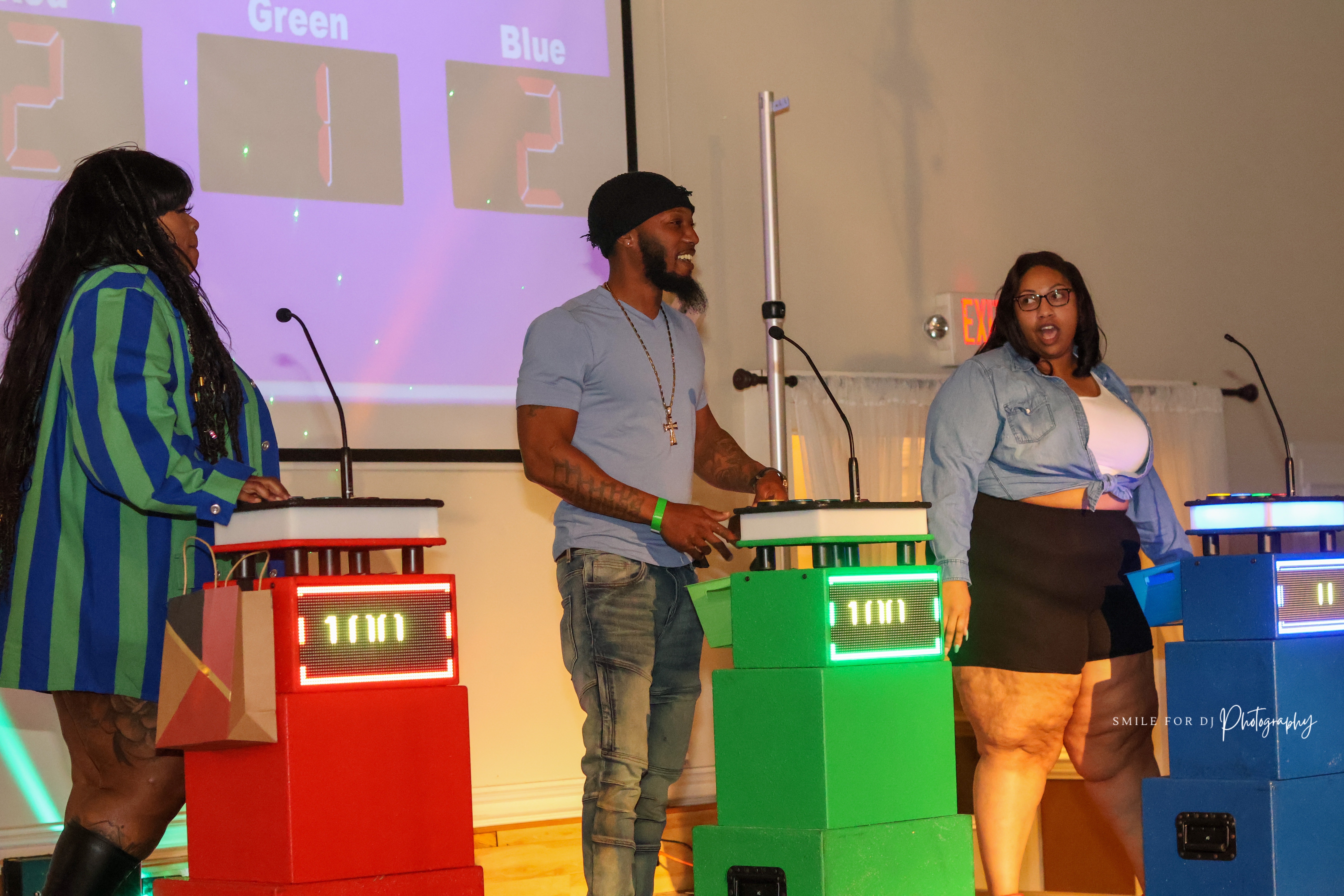Three contestants competing at red, green, and blue Black In The Day Trivia podiums