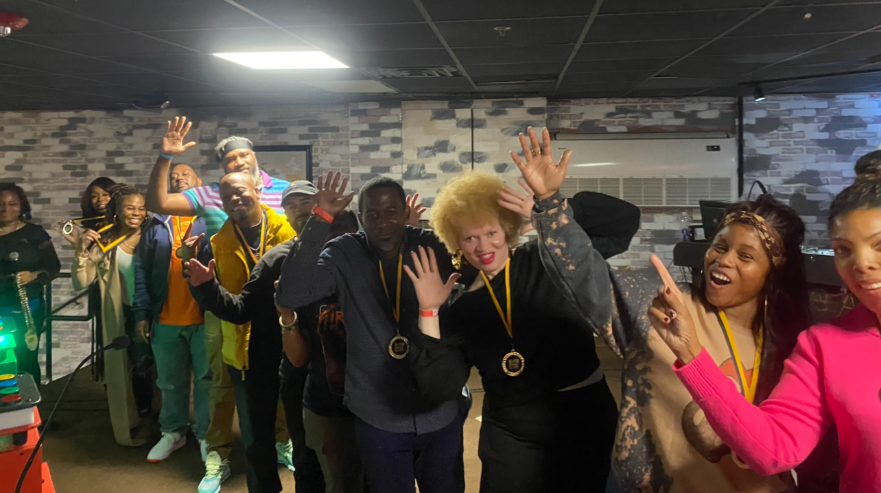 Guests wearing gold medals with their hands raised in celebration at a Black In The Day Trivia live show